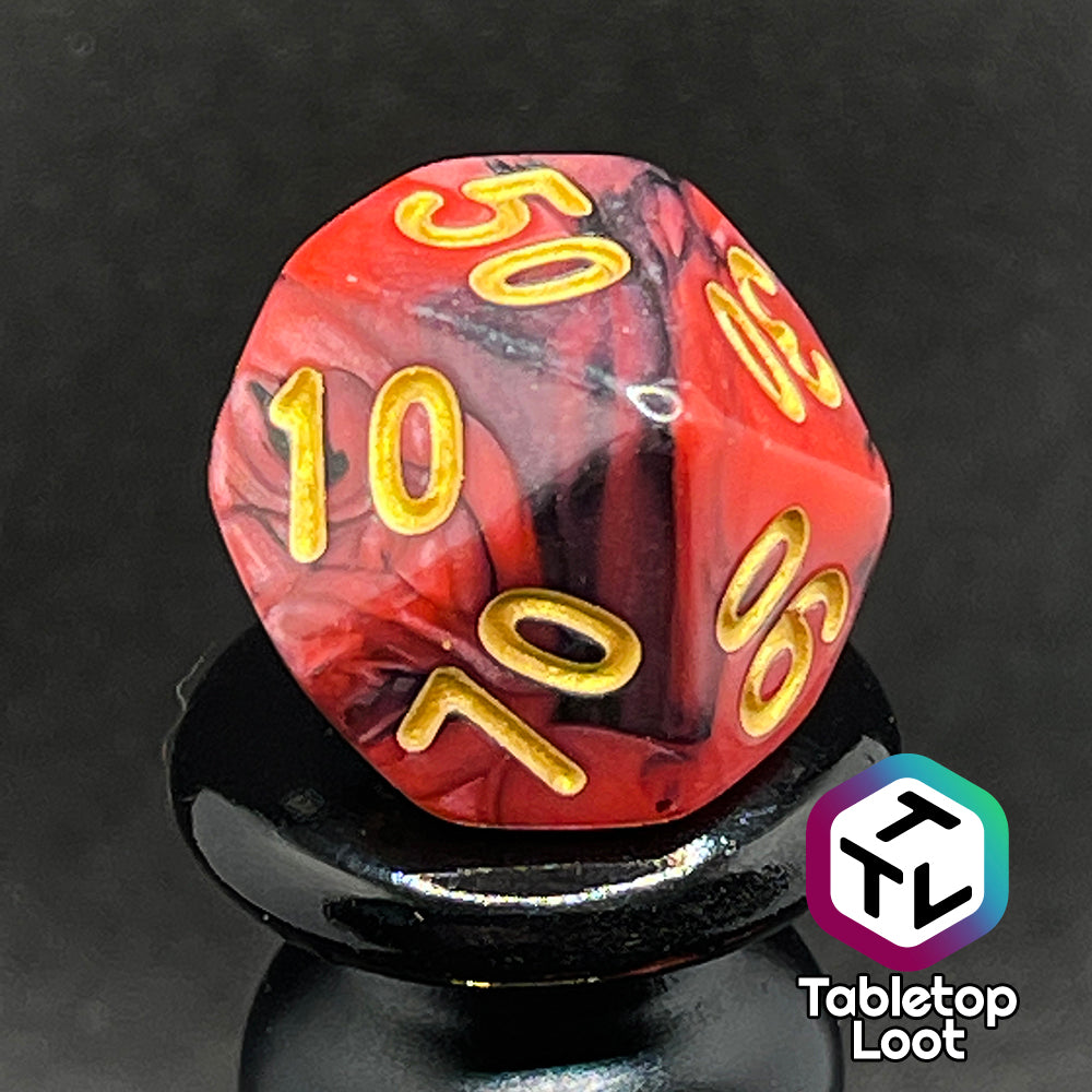 A close up of the percentile die from the Forge Embers 7 piece dice set with swirled black and red and gold numbering.