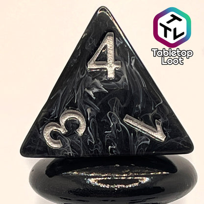 A close up of the D4 from the Form of Dread 7 piece dice set from Tabletop Loot with swirls of white in black resin and silver numbering.