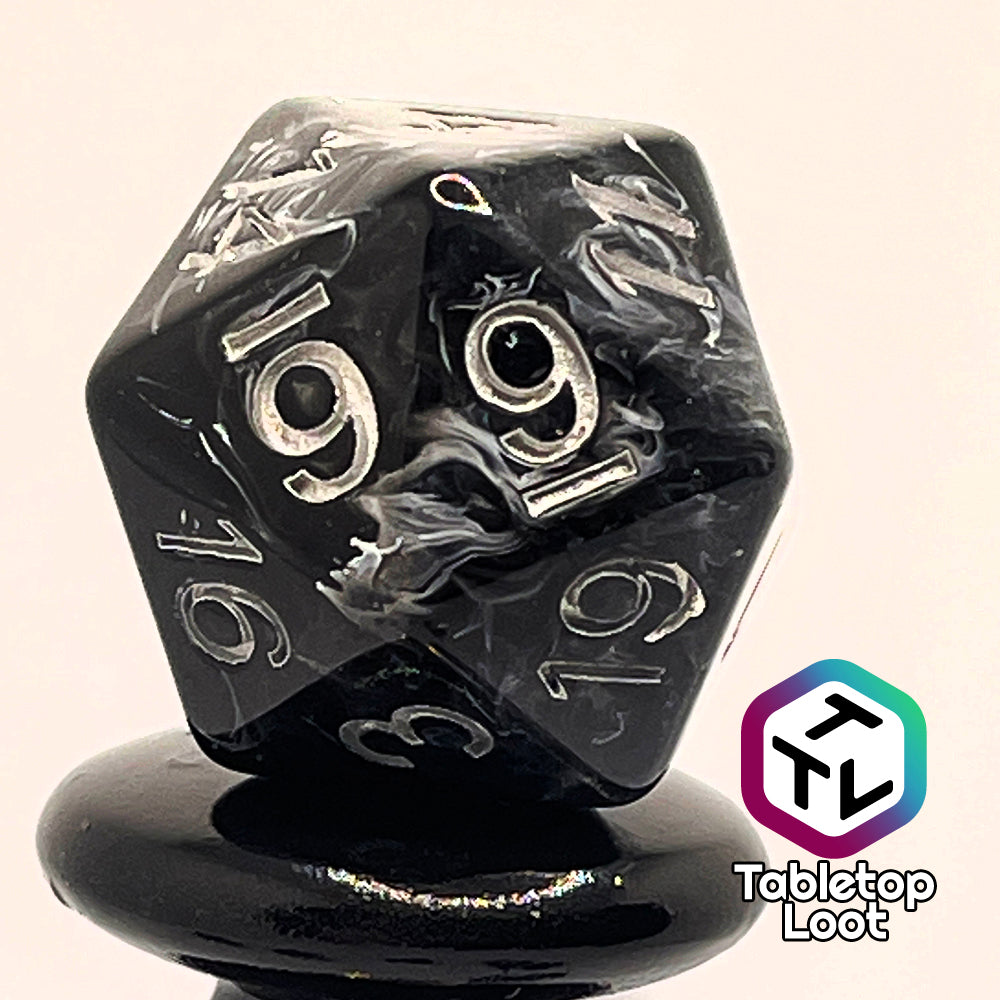 A close up of the D20 from the Form of Dread 7 piece dice set from Tabletop Loot with swirls of white in black resin and silver numbering.