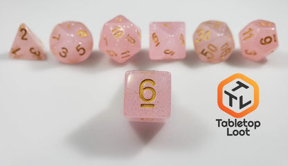 The Frosted Raspberry 7 piece dice set from Tabletop Loot with pastel pink glittery resin and gold numbering.