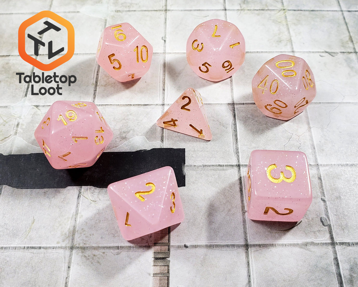 The Frosted Raspberry 7 piece dice set from Tabletop Loot with pastel pink glittery resin and gold numbering.