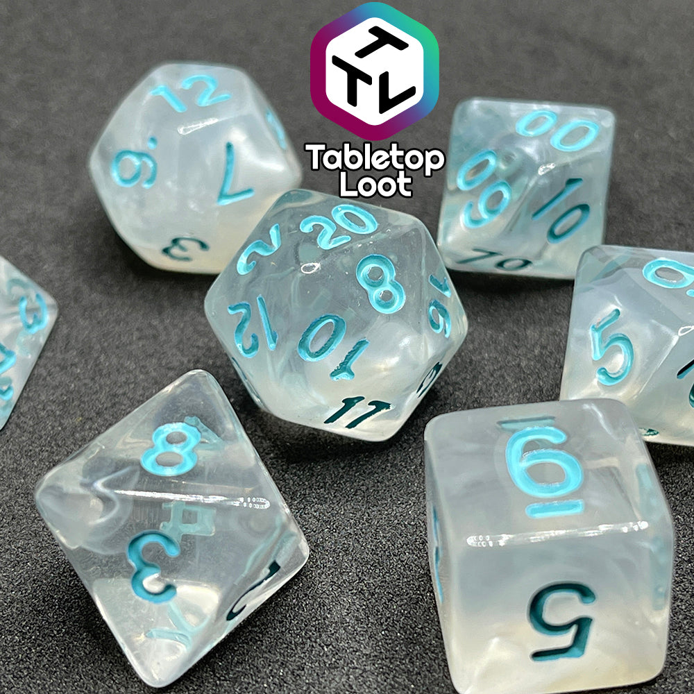 A close up of the Frostmaiden 7 piece dice set from Tabletop Loot with swirls of frosty white in clear resin and blue numbering.