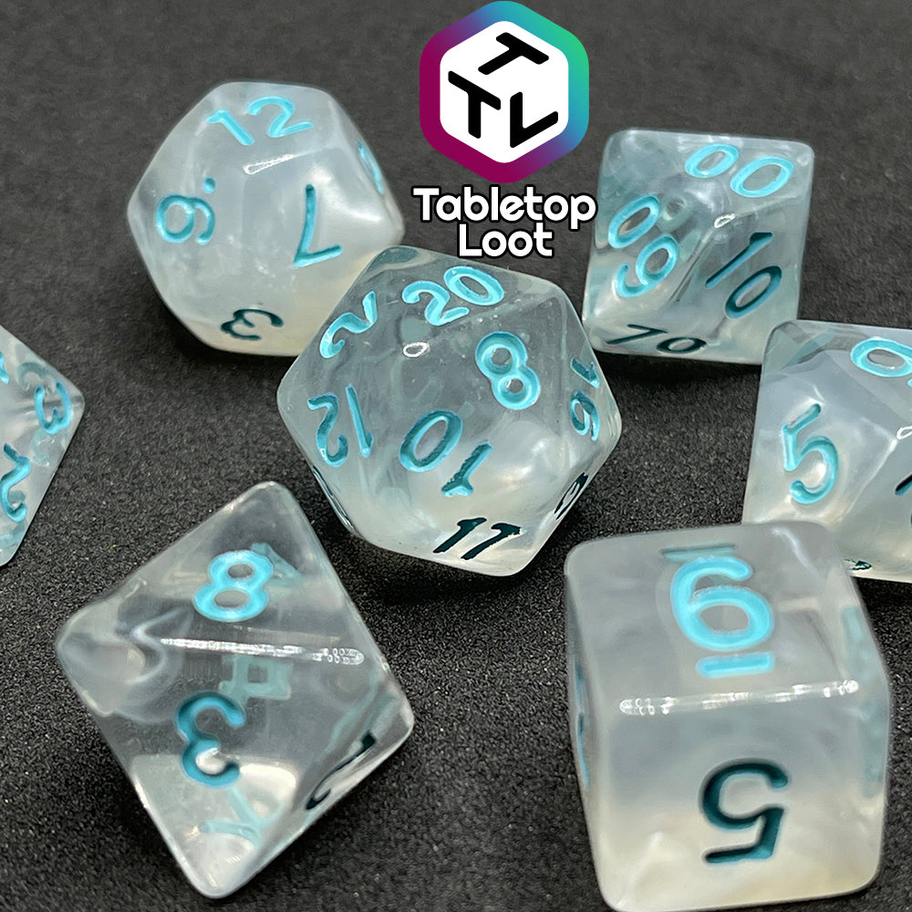 A close up of the Frostmaiden 7 piece dice set from Tabletop Loot with swirls of frosty white in clear resin and blue numbering.