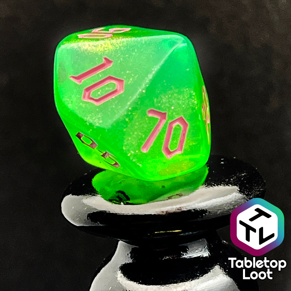 A close up of the percentile die from the Sour Apple 7 piece dice set from Tabletop Loot; shimmery green dice with pink gothic numbering.