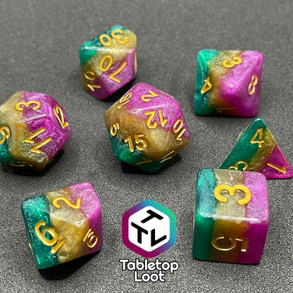 A close up of the Gem of Brightness 7 piece dice set from Tabletop Loot with stripes of glittery pink, gold, and green and inked in gold.