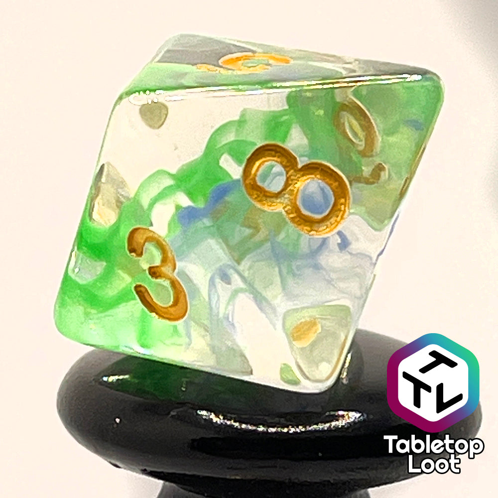 A close up of the D8 from the Gentle Repose 7 piece dice set with swirls of bright green and blue in clear resin and gold numbering.