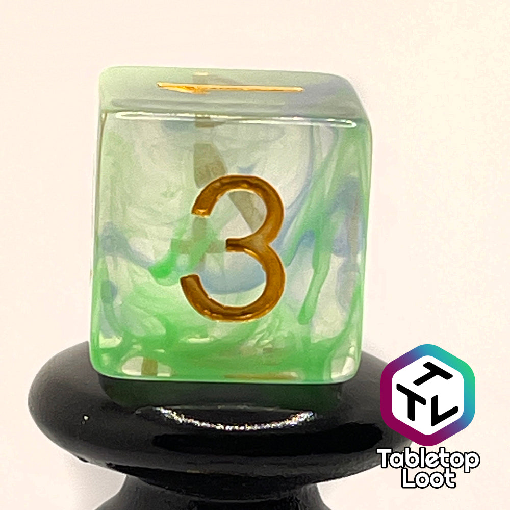 A close up of the D6 from the Gentle Repose 7 piece dice set with swirls of bright green and blue in clear resin and gold numbering.