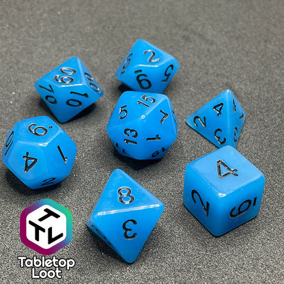 The Ghost Ice 7 piece dice set from Tabletop Loot with glowing blue pigment and black numbers, shown in the light.