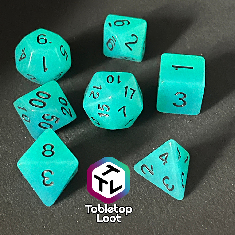 The Ghost Ice 7 piece dice set from Tabletop Loot with glowing blue pigment and black numbers, shown in the dark.