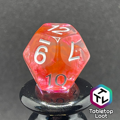 A close up of the D12 from the Healing Potion 7 piece dice set from Tabletop Loot; clear dice with swirls of orange and pink and white numbering.
