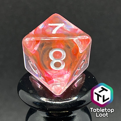 A close up of the D8 from the Healing Potion 7 piece dice set from Tabletop Loot; clear dice with swirls of orange and pink and white numbering.