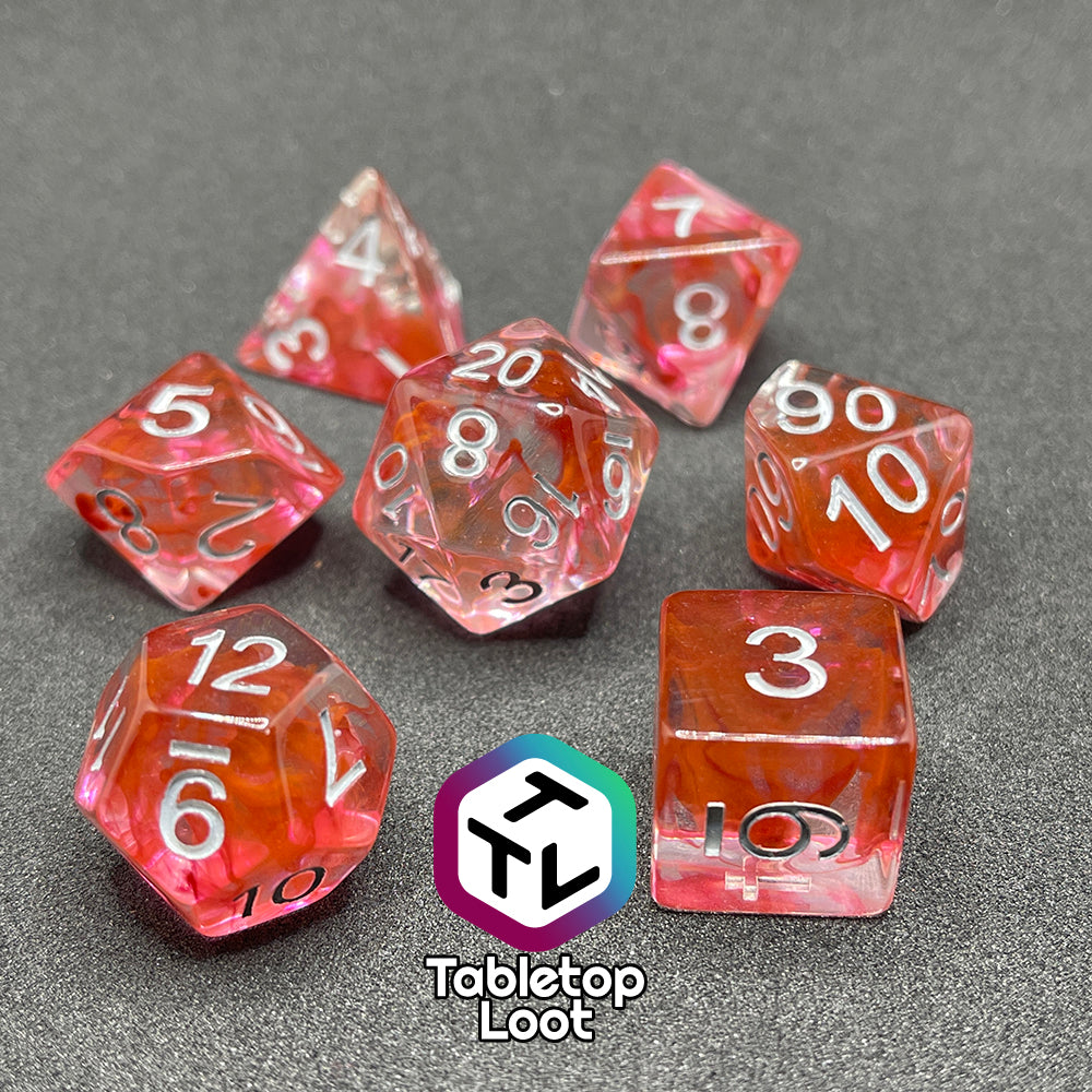 The Healing Potion 7 piece dice set from Tabletop Loot; clear dice with swirls of orange and pink and white numbering.