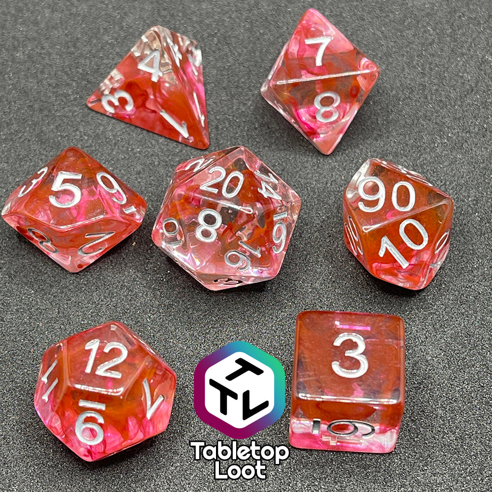 The Healing Potion 7 piece dice set from Tabletop Loot; clear dice with swirls of orange and pink and white numbering.