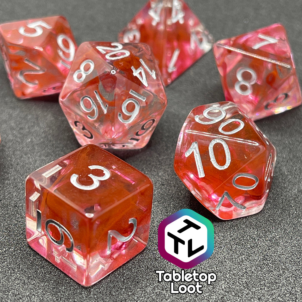 A close up of the Healing Potion 7 piece dice set from Tabletop Loot; clear dice with swirls of orange and pink and white numbering.