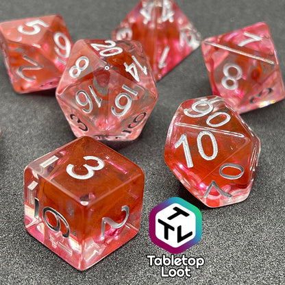 A close up of the Healing Potion 7 piece dice set from Tabletop Loot; clear dice with swirls of orange and pink and white numbering.