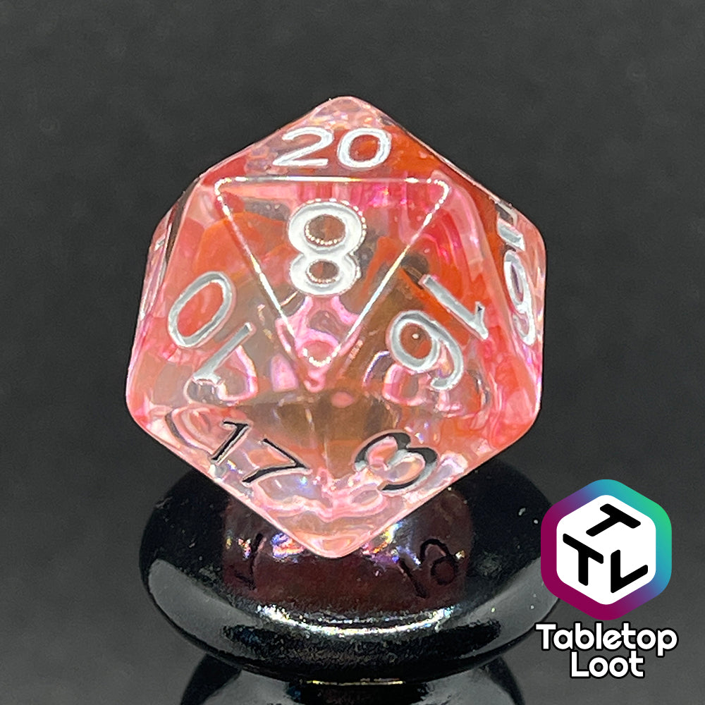 A close up of the D20 from the Healing Potion 7 piece dice set from Tabletop Loot; clear dice with swirls of orange and pink and white numbering.