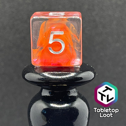 A close up of the D6 from the Healing Potion 7 piece dice set from Tabletop Loot; clear dice with swirls of orange and pink and white numbering.