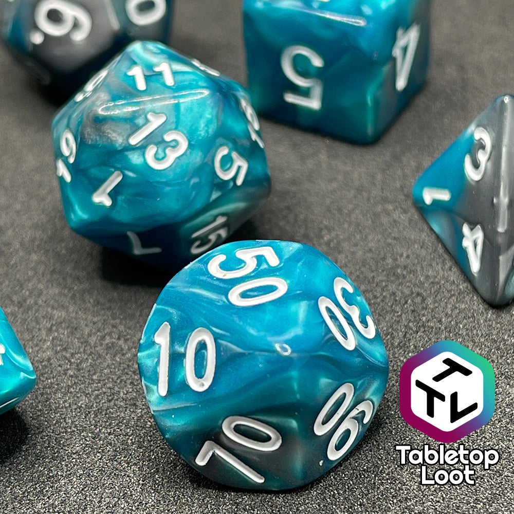 A close up of the percentile die from the Hunter's Mark 7 piece dice set from Tabletop Loot with pearlescent swirls of blue and silver and white numbering.