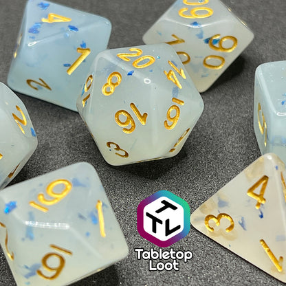 A close up of the Ice Shards 7 piece dice set from Tabletop Loot with blue metal flakes in milky white resin with gold numbering.
