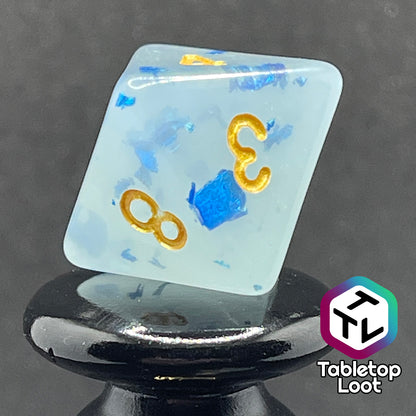 A close up of the D8 from the Ice Shards 7 piece dice set from Tabletop Loot with blue metal flakes in milky white resin with gold numbering.