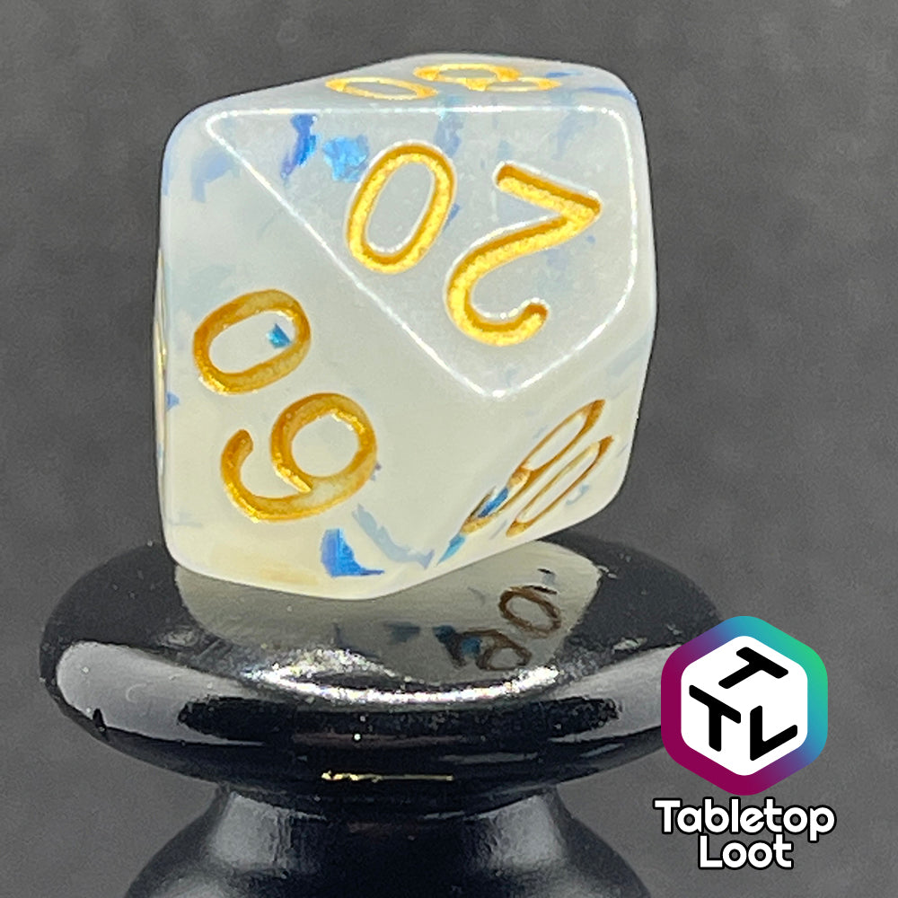 A close up of the percentile die from the Ice Shards 7 piece dice set from Tabletop Loot with blue metal flakes in milky white resin with gold numbering.