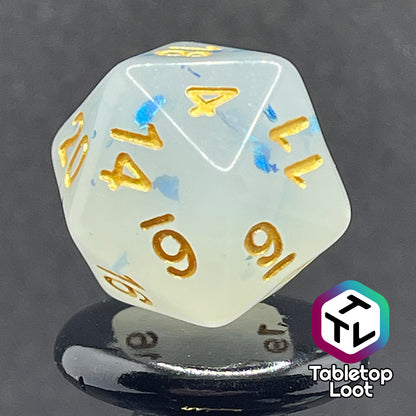 A close up of the D20 from the Ice Shards 7 piece dice set from Tabletop Loot with blue metal flakes in milky white resin with gold numbering.