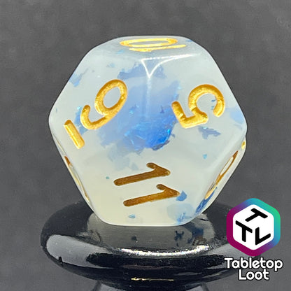 A close up of the D12 from the Ice Shards 7 piece dice set from Tabletop Loot with blue metal flakes in milky white resin with gold numbering.