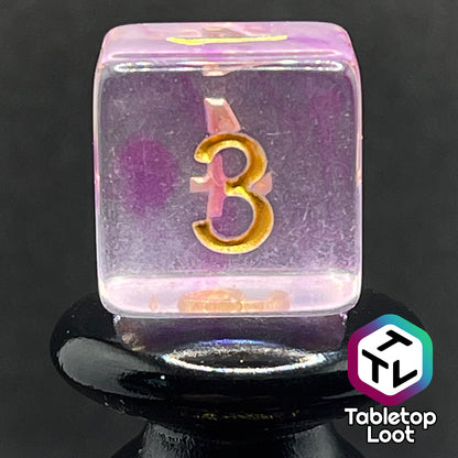 A close up of the D6 from the Incantation 7 piece dice set from Tabletop Loot with swirls of fuchsia in clear and gold numbering.