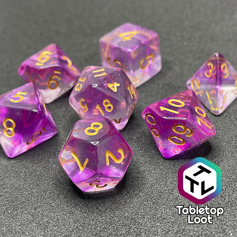 A close up of the Incantation 7 piece dice set from Tabletop Loot with swirls of fuchsia in clear and gold numbering.