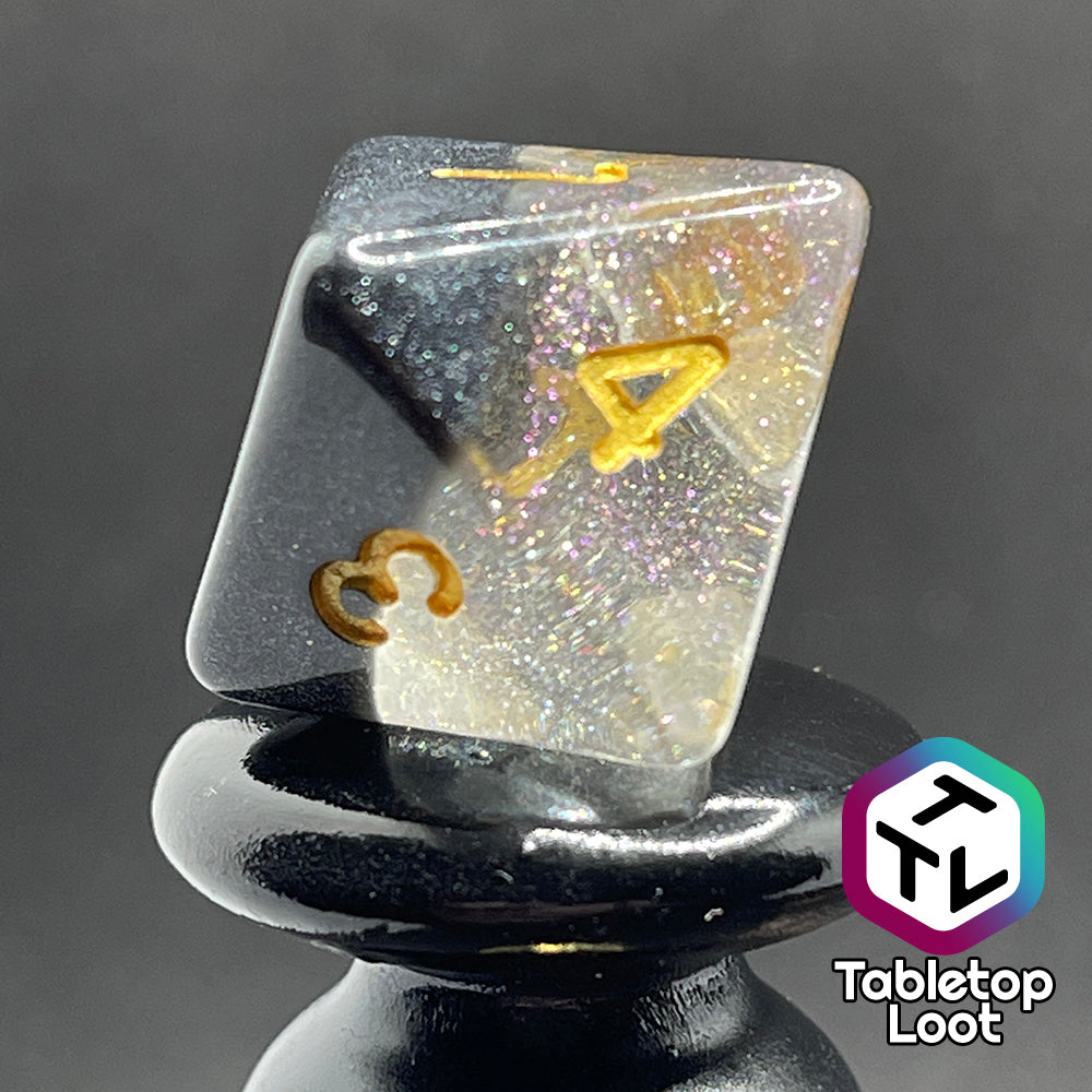 A close up of the D8 from the Inkwell 7 piece dice set from Tabletop Loot with a layer of black glittery color on clear glittery resin and gold numbering.