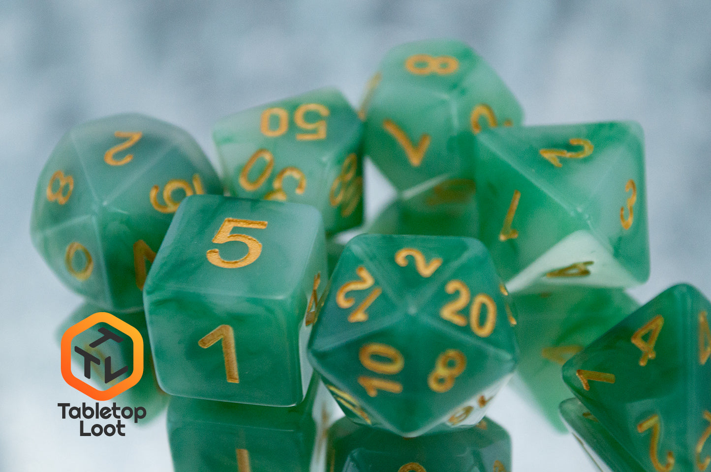A close up of the Jade 7 piece dice set from Tabletop Loot with swirls of jade green and white resin and gold numbering.