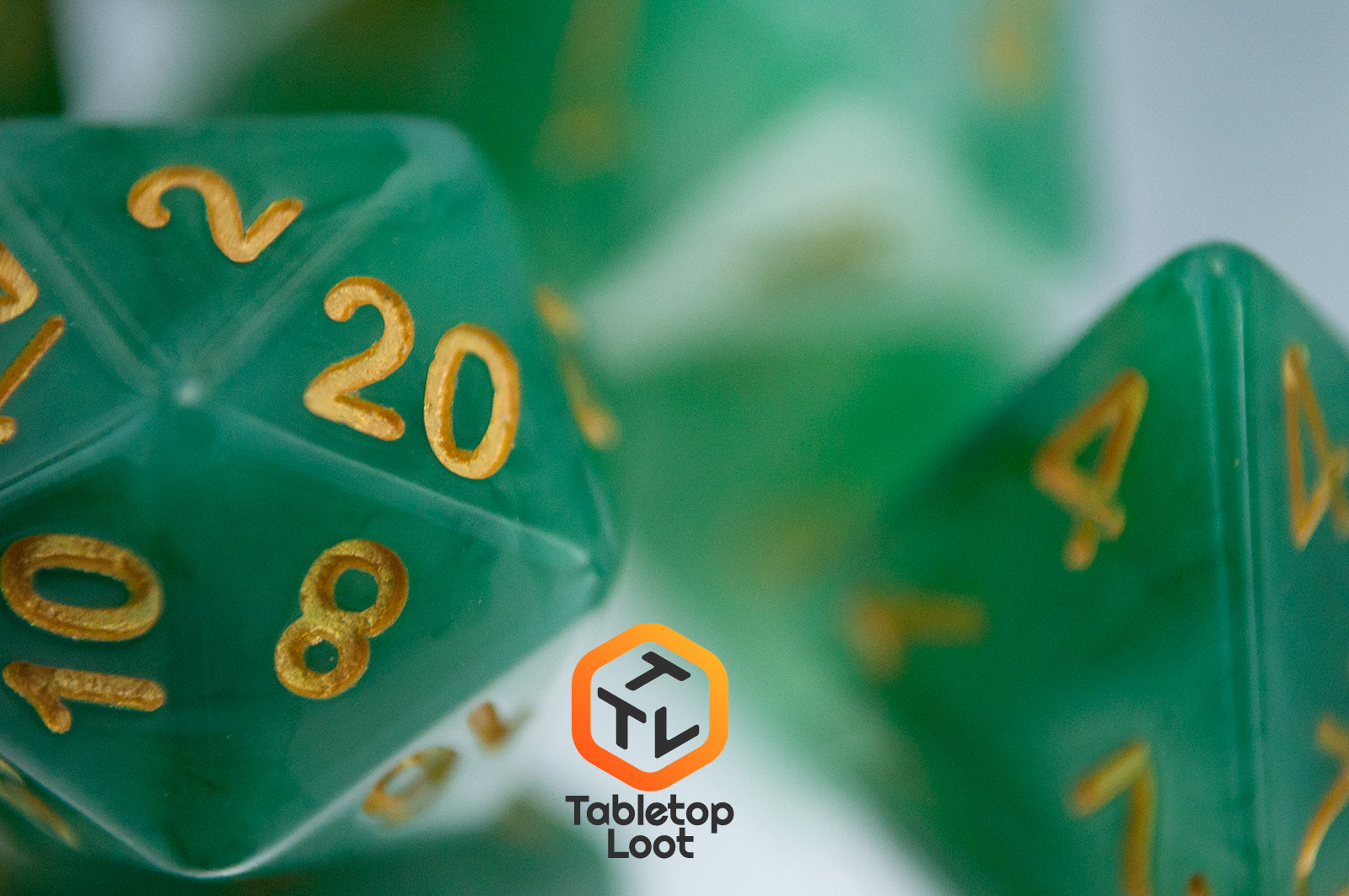 A close up of the Jade 7 piece dice set from Tabletop Loot with swirls of jade green and white resin and gold numbering.