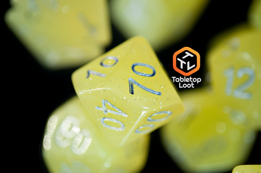 A close up of the Lemon Drops 7 piece dice set from Tabletop Loot; bright yellow with silver glitter and numbering.