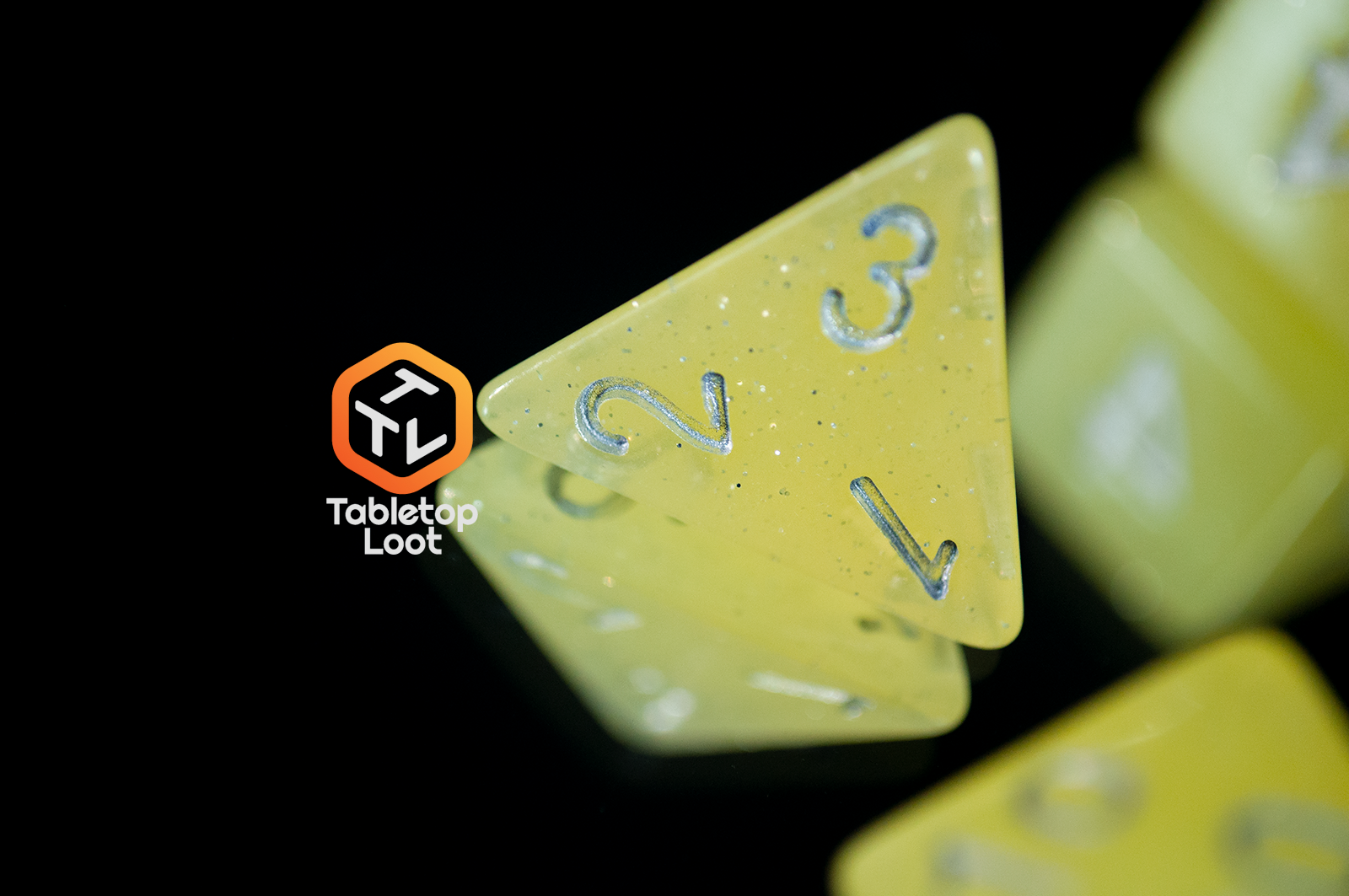 A close up of the D4 from the Lemon Drops 7 piece dice set from Tabletop Loot; bright yellow with silver glitter and numbering.