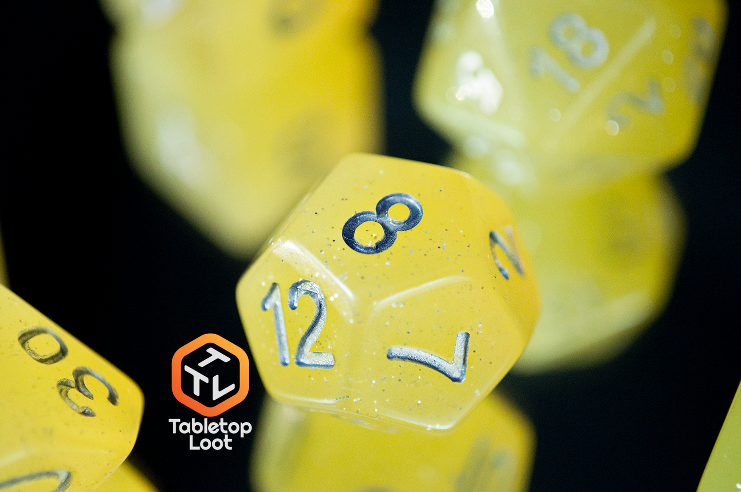 A close up of the D12 from the Lemon Drops 7 piece dice set from Tabletop Loot; bright yellow with silver glitter and numbering.