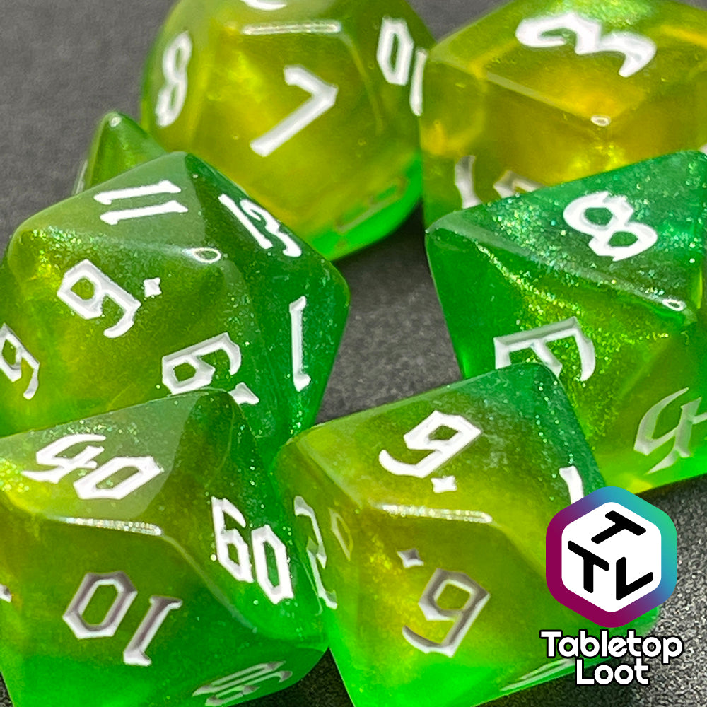 A close up of the Luck 7 piece dice set from Tabletop Loot; translucent green and yellow swirled with micro glitter and white gothic numbering.