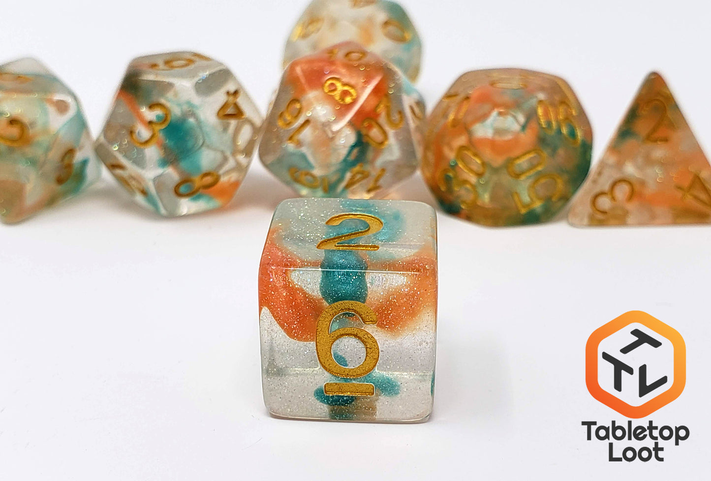 A close up of the Luminous Koi 7 piece dice set from Tabletop Loot with swirls of orange and blue in a clear glittery resin with gold numbering.