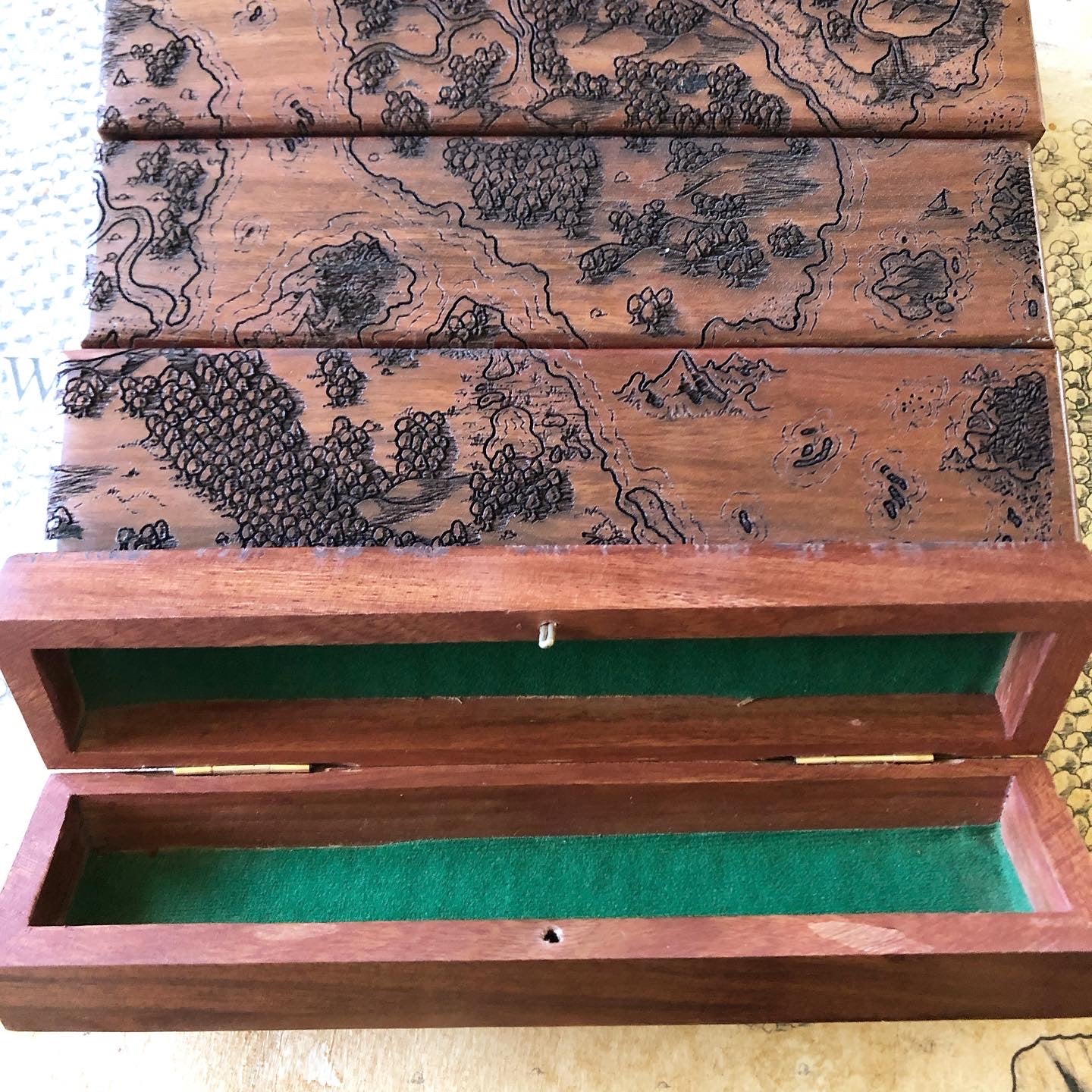 A collection of wood dice vaults lined up to show the parts of a Deven Rue world map burned into the tops, the last in line open to show a forest green liner.