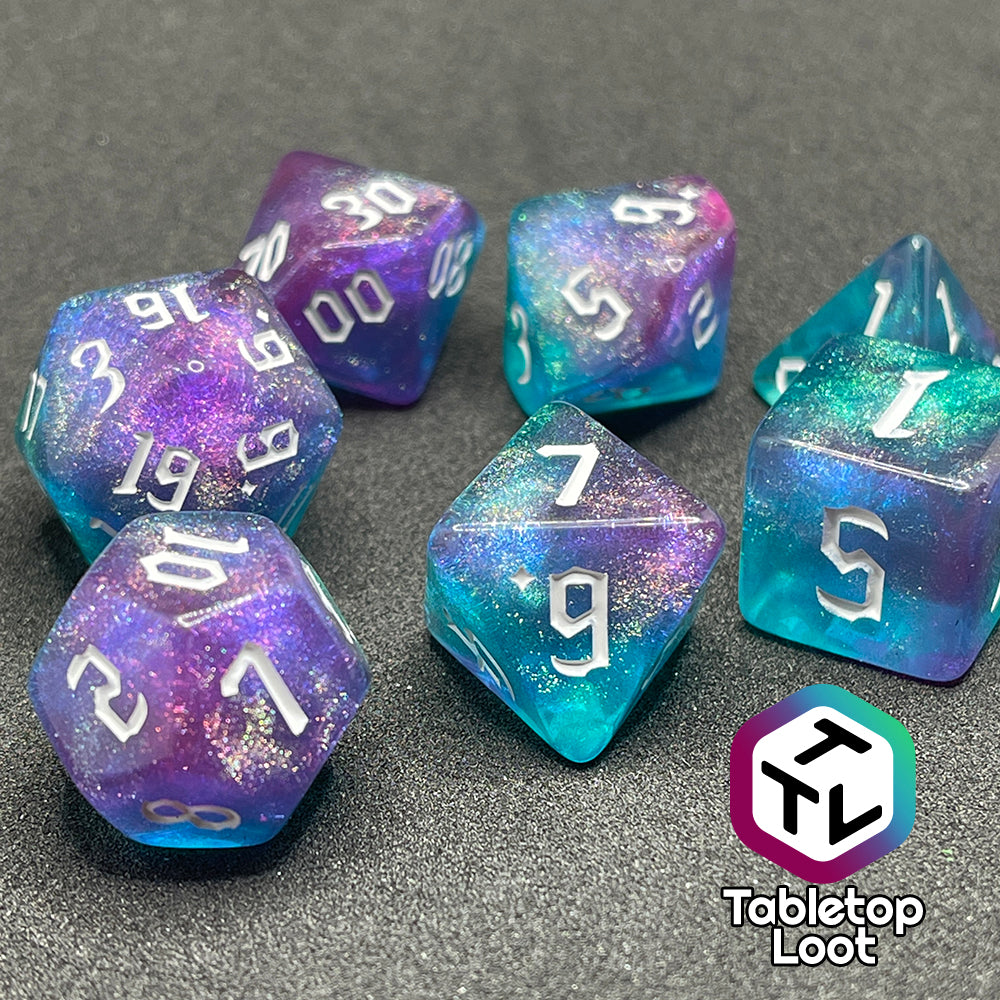 A close up of the Mermaid Lagoon 7 piece dice set from Tabletop Loot with shimmery swirls of blue and purple and white gothic numbering.