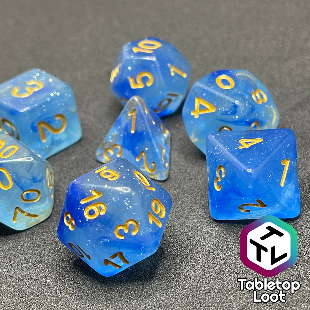 A close up of the Mermaid's Crown 7 piece dice set from Tabletop Loot with swirled blue tones, tons of glitter, and gold numbering.