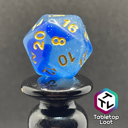 A close up of the D20 from the Mermaid's Crown 7 piece dice set from Tabletop Loot with swirled blue tones, tons of glitter, and gold numbering.
