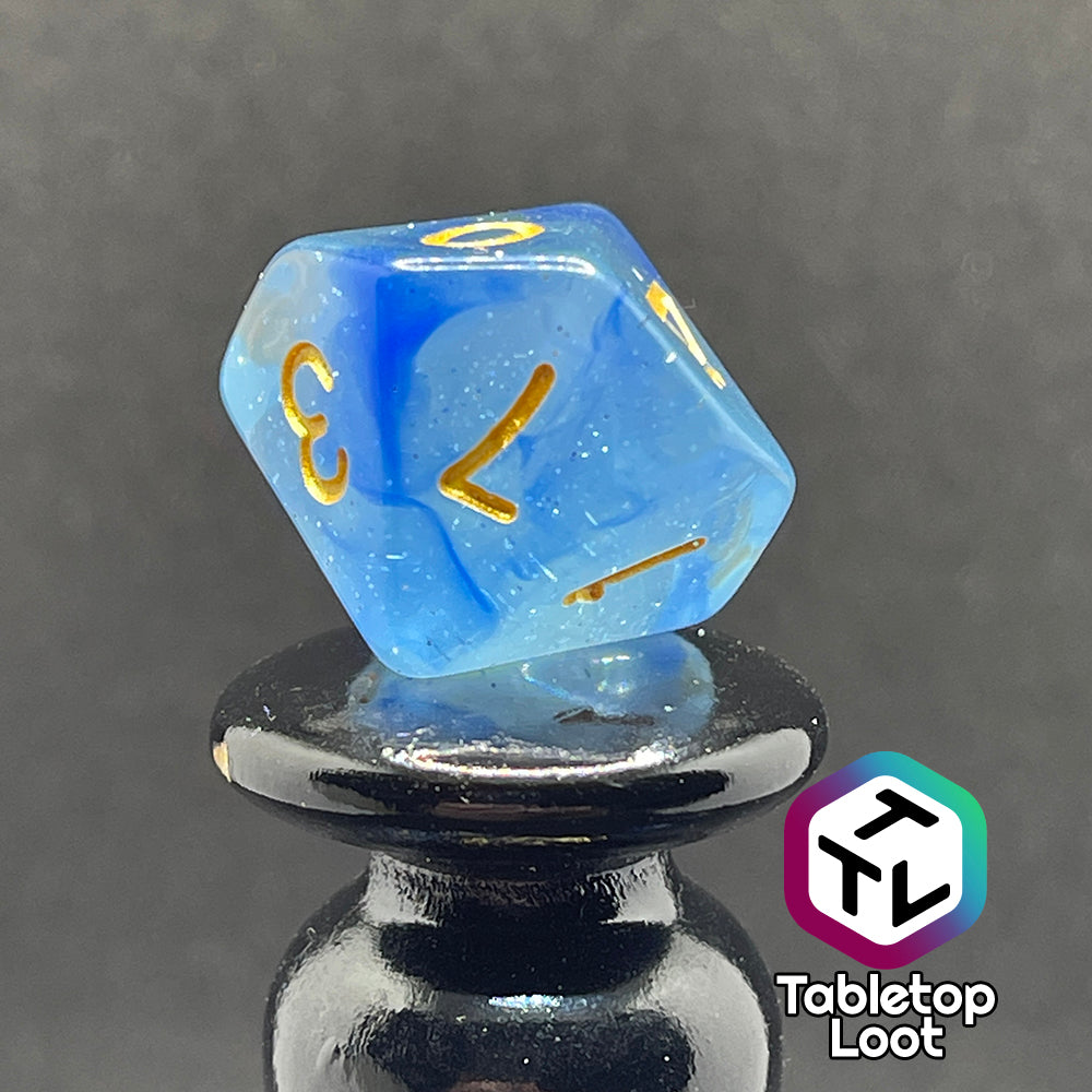 A close up of the percentile die from the Mermaid's Crown 7 piece dice set from Tabletop Loot with swirled blue tones, tons of glitter, and gold numbering.