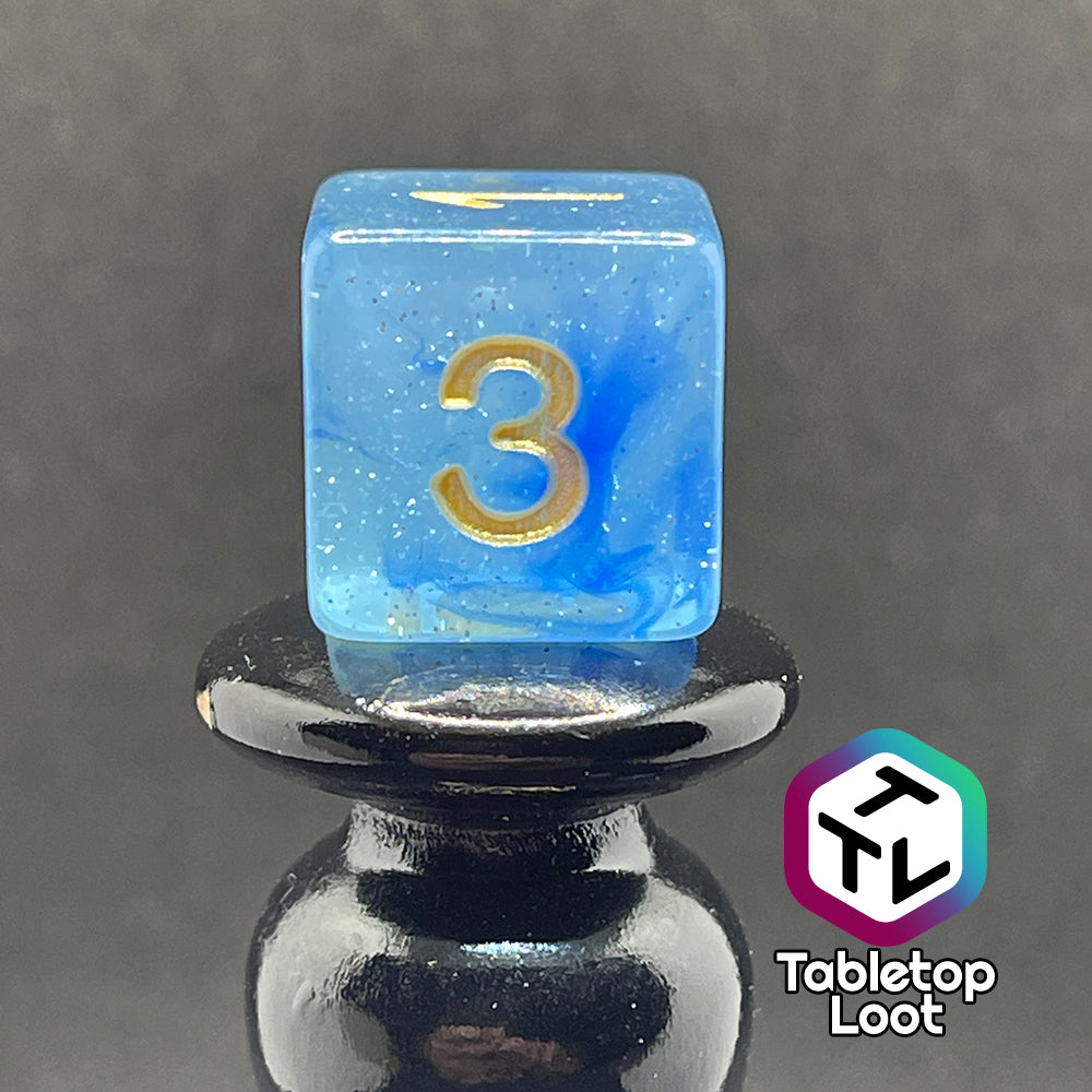 A close up of the D6 from the Mermaid's Crown 7 piece dice set from Tabletop Loot with swirled blue tones, tons of glitter, and gold numbering.