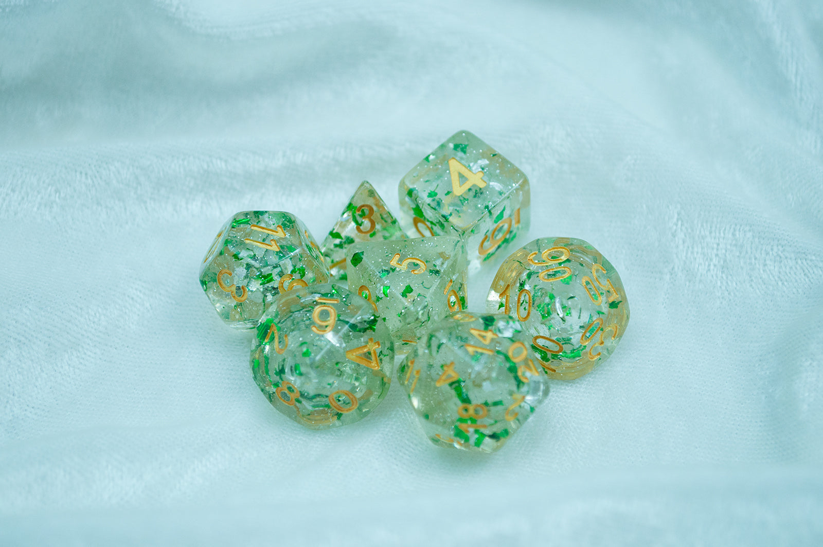 The Metallic Emerald 7 piece dice set from Tabletop Loot with green metallic flakes suspended in clear resin with glitter and gold numbering.