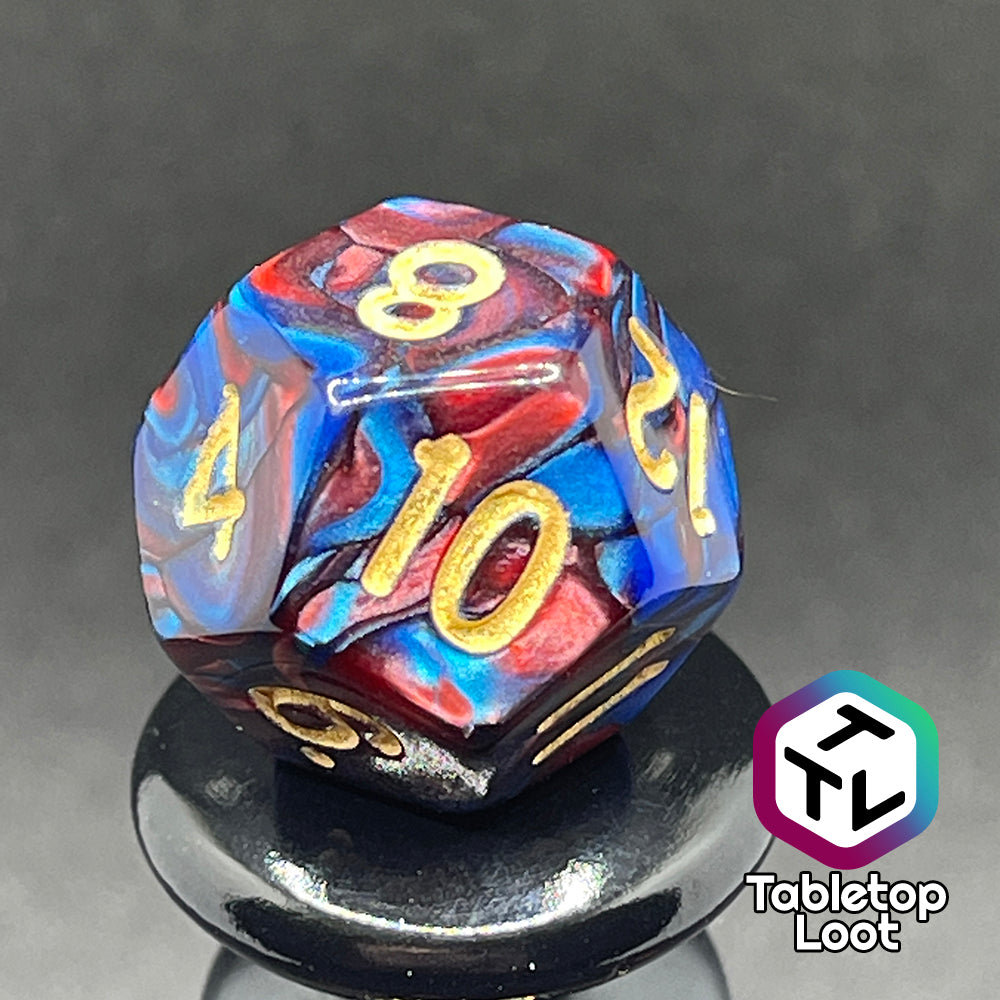 A close up of the D12 from the Metropolis 7 piece dice set with swirls of pearlescent blue and red and gold numbering.