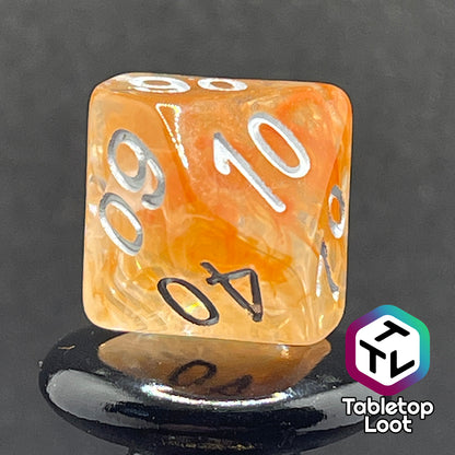 Another angle close up of the percentile die from the Hunter's Moon 7 piece dice set from Tabletop Loot with swirls of orange and white in clear resin and white numbering.