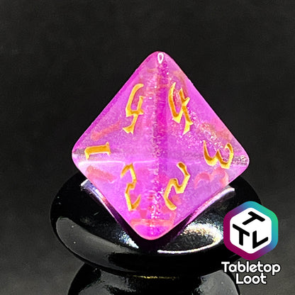 A close up of the D4 from the Moxie 7 piece dice set from Tabletop Loot; fuchsia dice packed with glitter and gold gothic numbering.