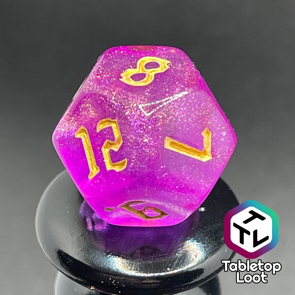 Another angle of close up of the D12 from the Moxie 7 piece dice set from Tabletop Loot; fuchsia dice packed with glitter and gold gothic numbering.