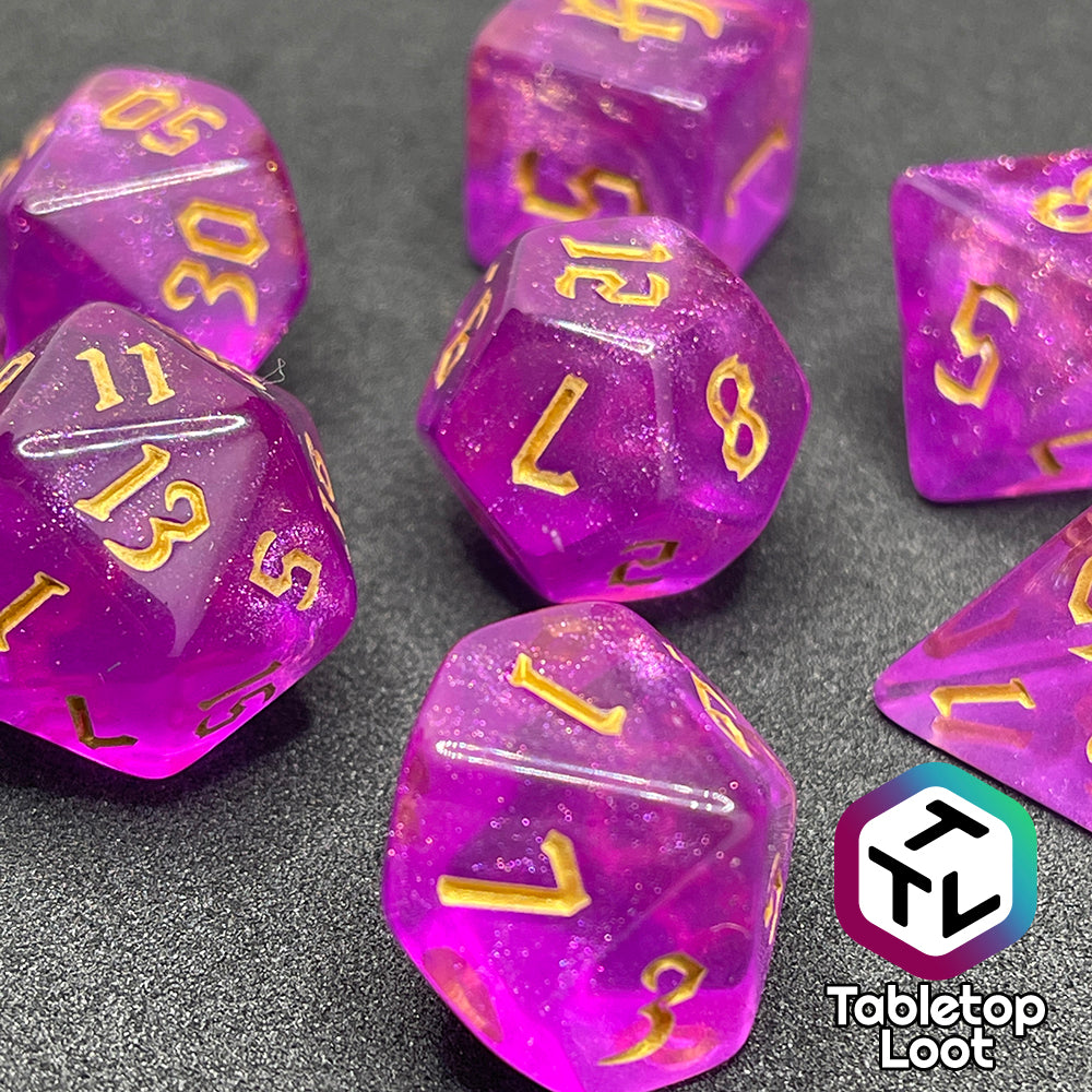 A close up of the Moxie 7 piece dice set from Tabletop Loot; fuchsia dice packed with glitter and gold gothic numbering.