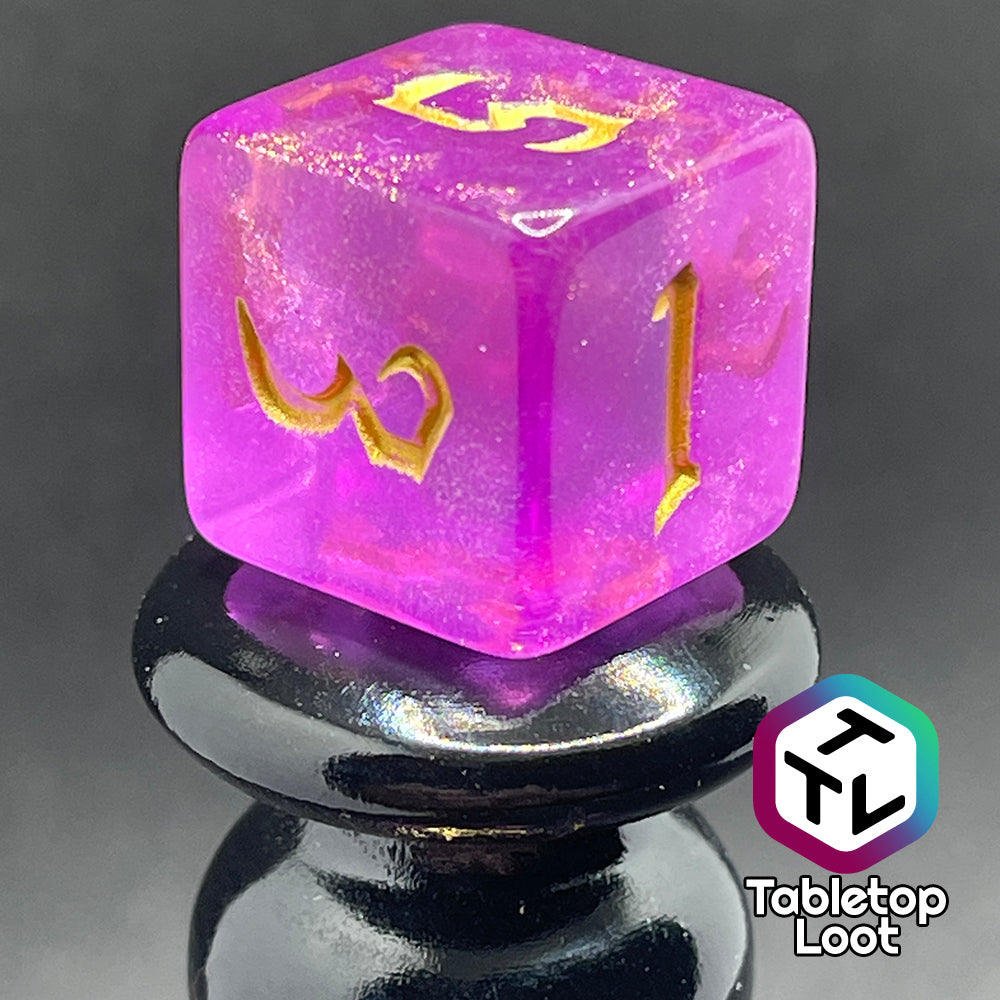 A close up of the D6 from the Moxie 7 piece dice set from Tabletop Loot; fuchsia dice packed with glitter and gold gothic numbering.
